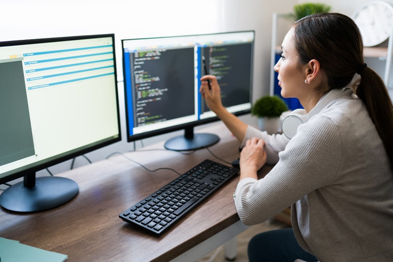 Woman coding on dual monitors, MERN stack training and full stack development career opportunities.