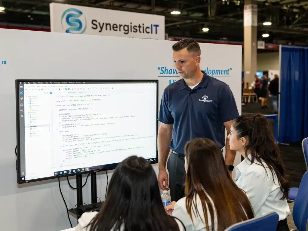 SynergisticIT representative presenting software development training to candidates at a conference.