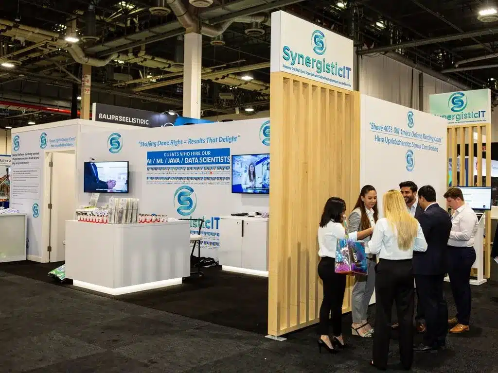 SynergisticIT trade show booth with clients and staff discussing IT staffing and technology upskilling solutions.