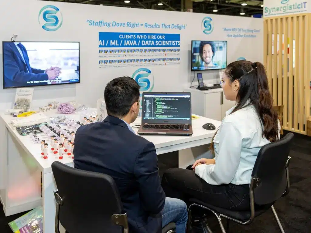 SynergisticIT booth showcasing AI, ML, Java, and Data Scientists talent, with recruiters assisting candidates.